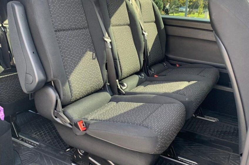 A car's interior with two front seats, seat belts, and a rearview mirror. 3