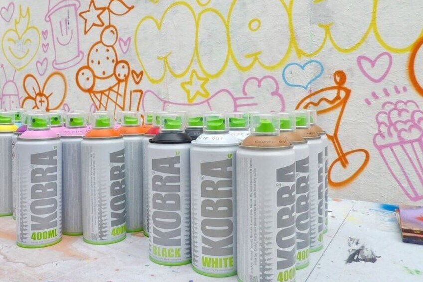 Cans of Cobra energy drink in various colors lined up against a wall with colorful graffiti. 1