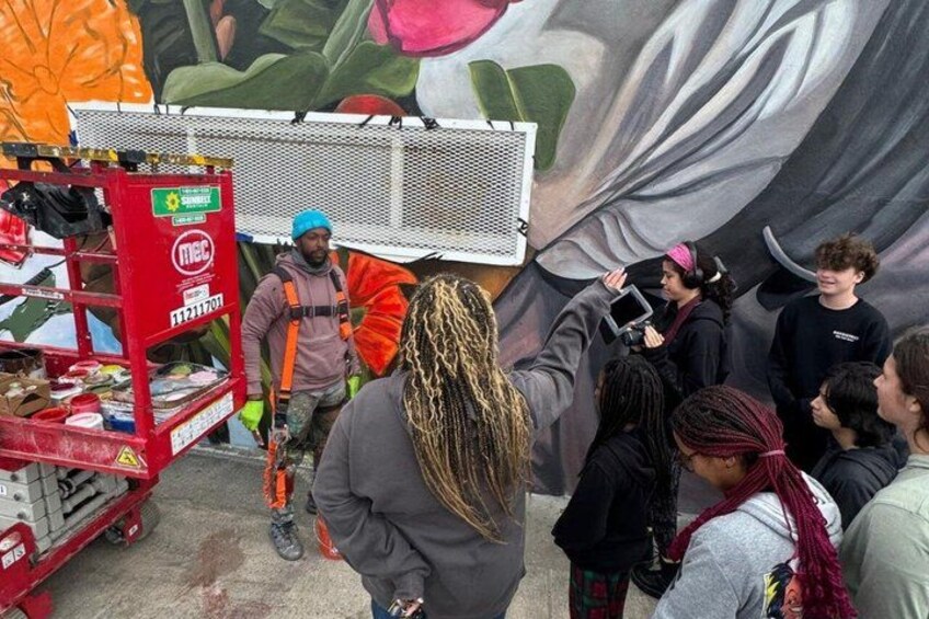 A mural with a person taking a photo, a red vending machine, and a crowd of people. 4