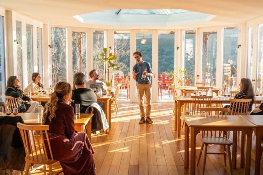 A restaurant with wooden tables and chairs, large windows, and a person standing in the center. 3