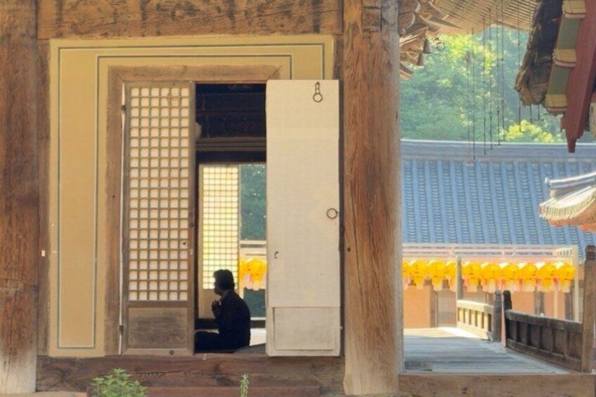 A person sitting inside a traditional building with a wooden door and a view of a temple with yellow decorations. 3