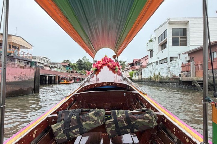 A narrow boat with a canopy, decorated with flowers, moving through a canal with buildings on either side. 1