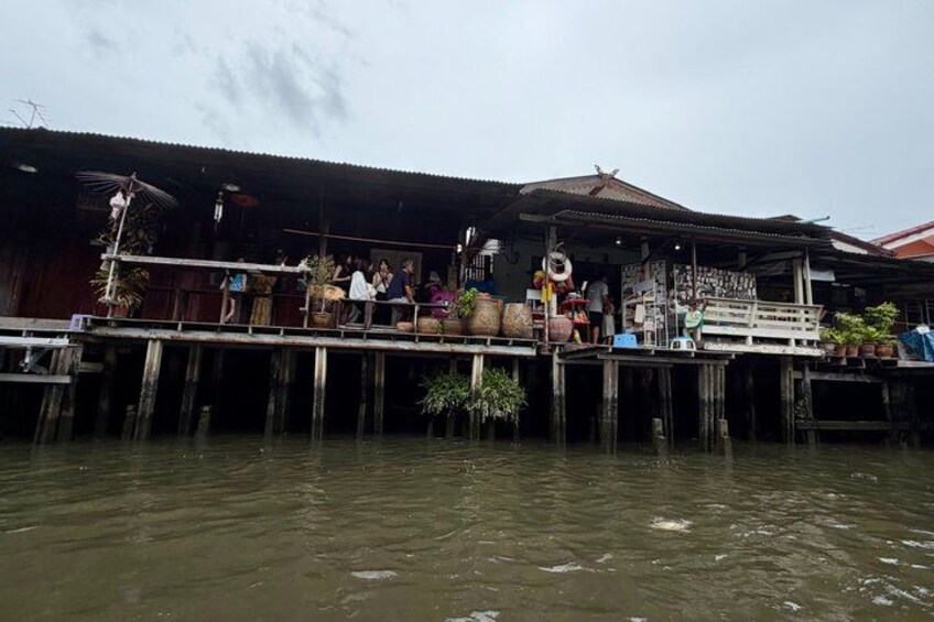 A wooden structure extending over water with people on the deck, surrounded by plants and a cloudy sky. 2