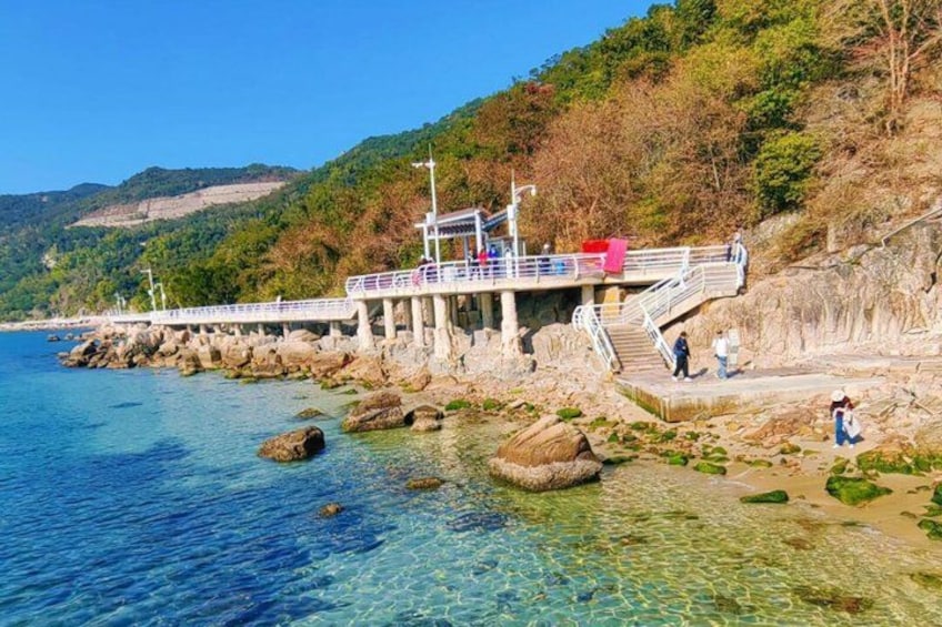 A pier extending into a clear blue lake with rocky shores, surrounded by hills and trees. 2