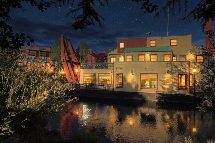 A waterfront building with illuminated windows and a red sculpture. 1