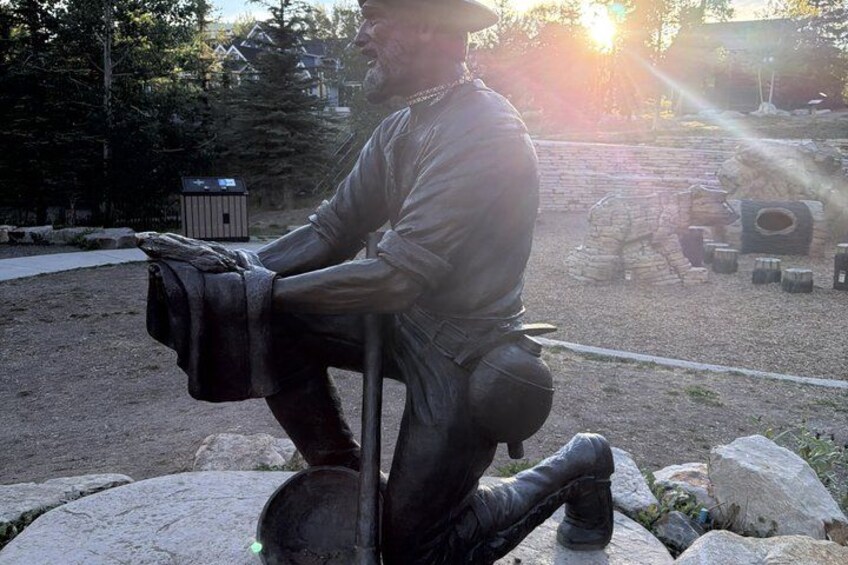 A statue of a man sitting on a rock with a bag, surrounded by stones and a small structure in the background. 5