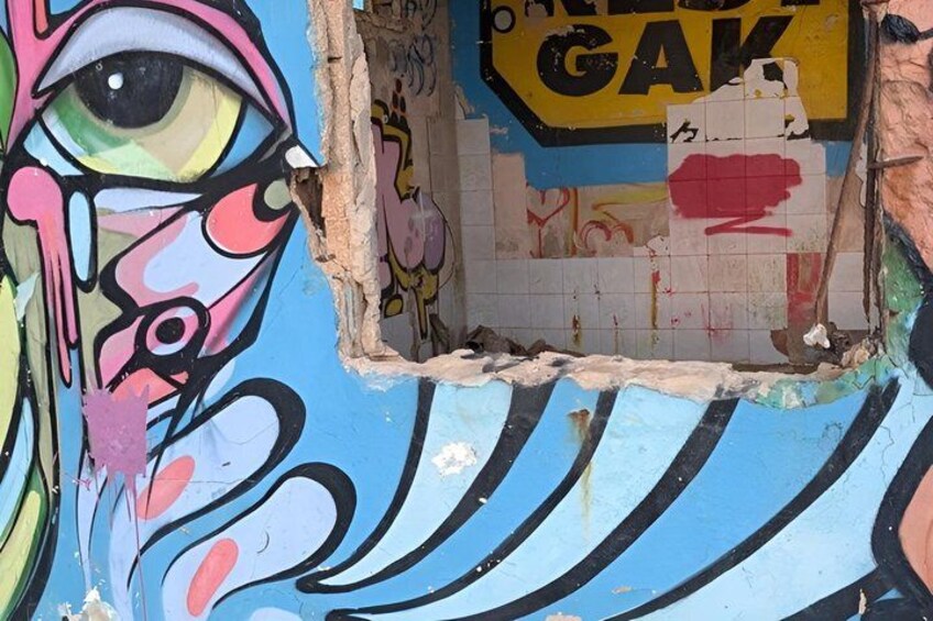 A wall with graffiti, including a prominent eye design and a sign that reads 'GAK.' 2