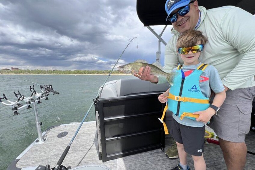 A person holding a fish on a boat with fishing rods and a cooler. 2