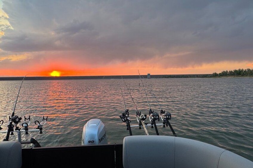 A boat with fishing rods, a white motor, and a sunset over the water. 4
