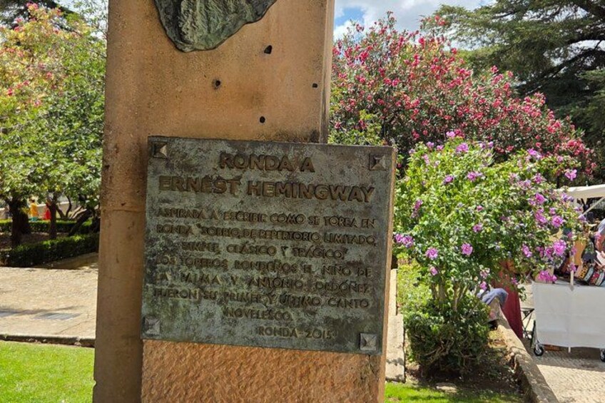 A plaque on a column with text in a foreign language, surrounded by greenery and flowers. 3