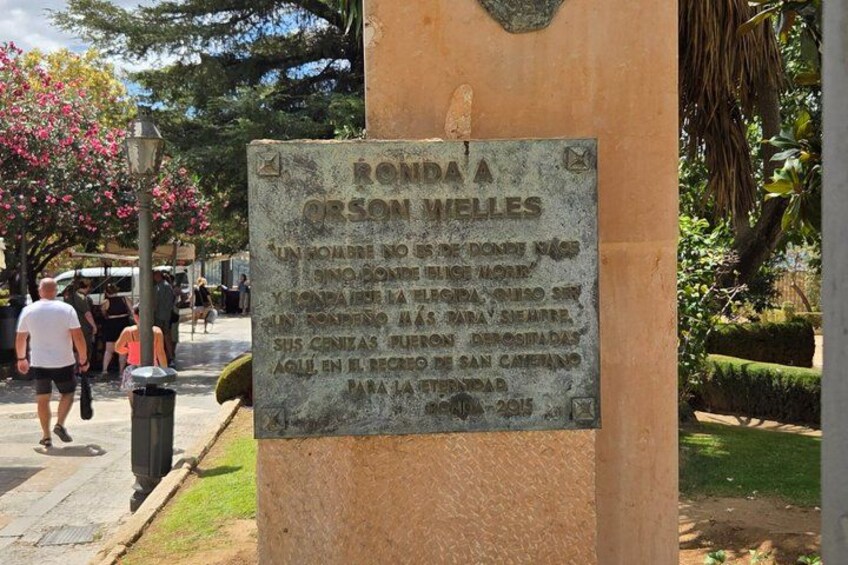 A stone plaque with inscriptions, a paved walkway, and a person walking in the background. 2