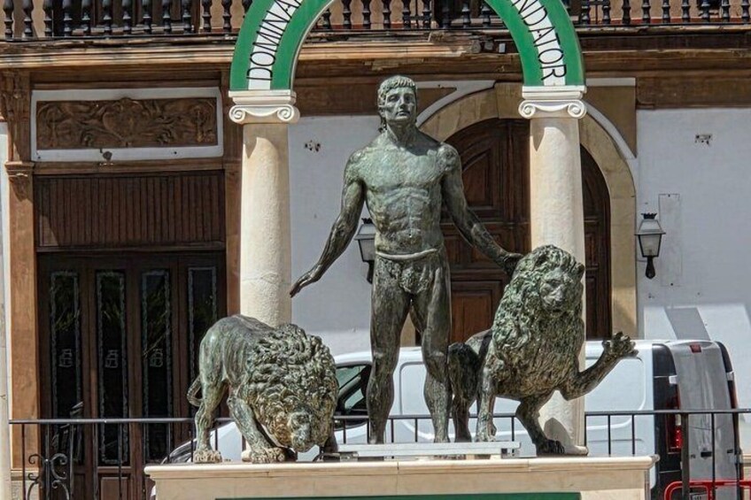 A statue of a man with two animals, a lion and a bear, in front of a building with a green archway. 5