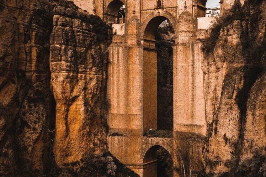 A historical stone bridge with arches, set against a rocky cliff. 1