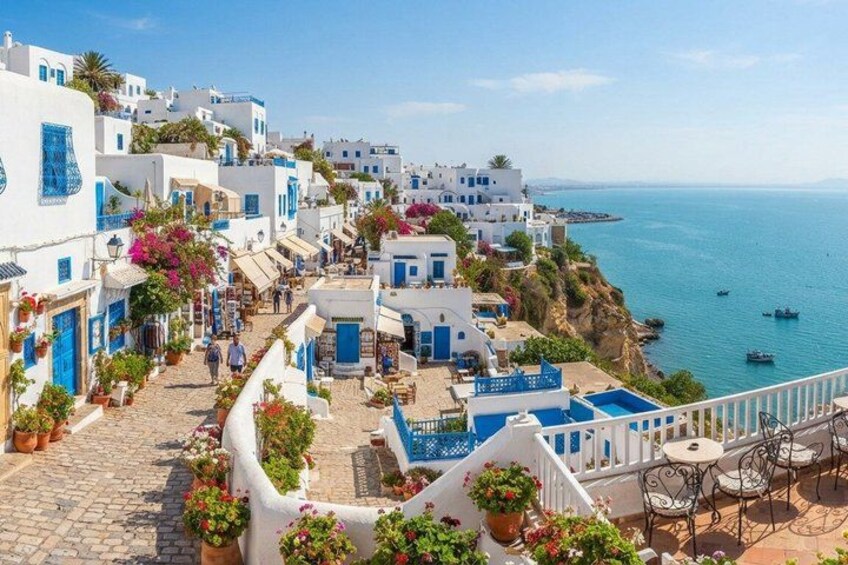 A coastal village with white buildings, blue doors, and a clear blue sea. 1