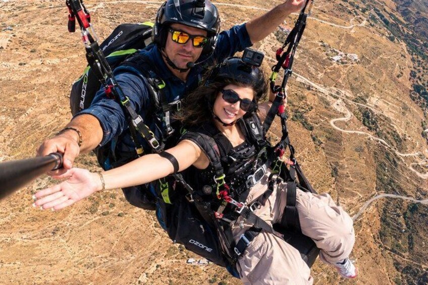 A person skydiving with a parachute, another person assisting, and a mountainous landscape below. 1