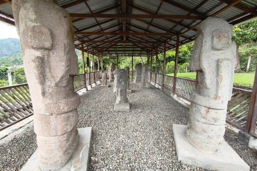 A covered walkway with stone statues, gravel ground, and a metal railing. 5