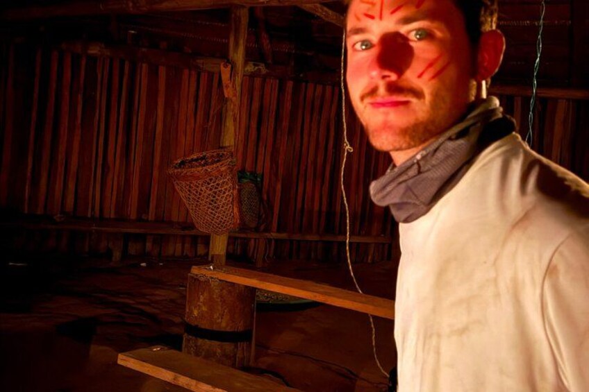 A person in a white shirt standing indoors with a wooden background and a basket hanging on a pole. 1