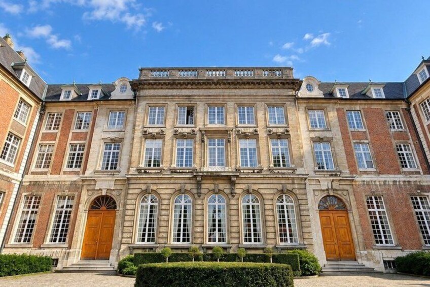 A historic building with multiple windows, a central entrance, and a well-maintained hedge in front. 5