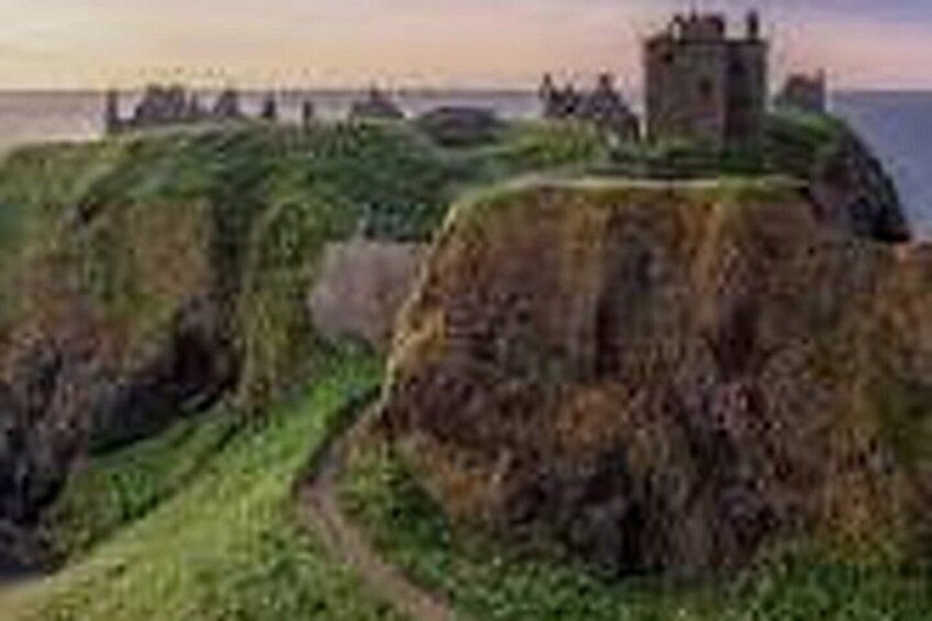 A coastal landscape with a castle on a grassy hill, cliffs, and the sea in the background. 3