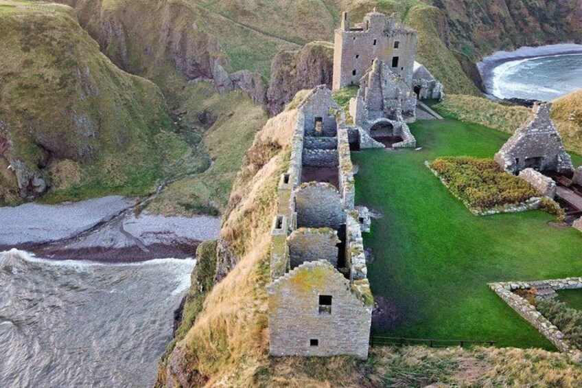 A coastal castle ruins with a grassy lawn and a cliffside view. 2