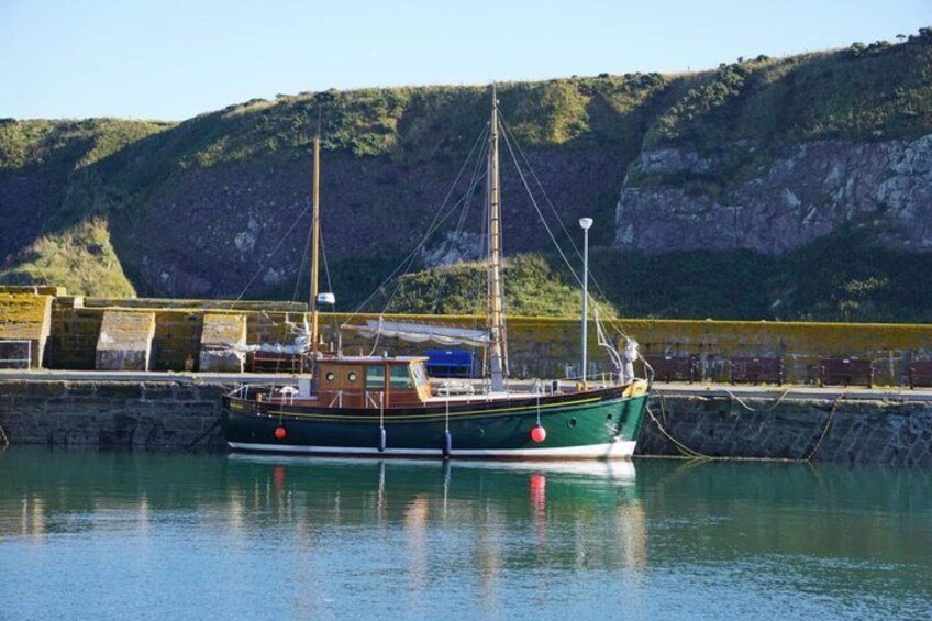 A green boat docked at a harbor with a rocky cliff in the background. 4