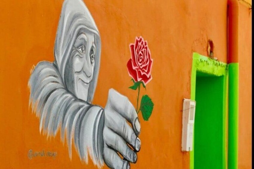 A mural of a hand holding a rose on a wall with a green door in the background. 4