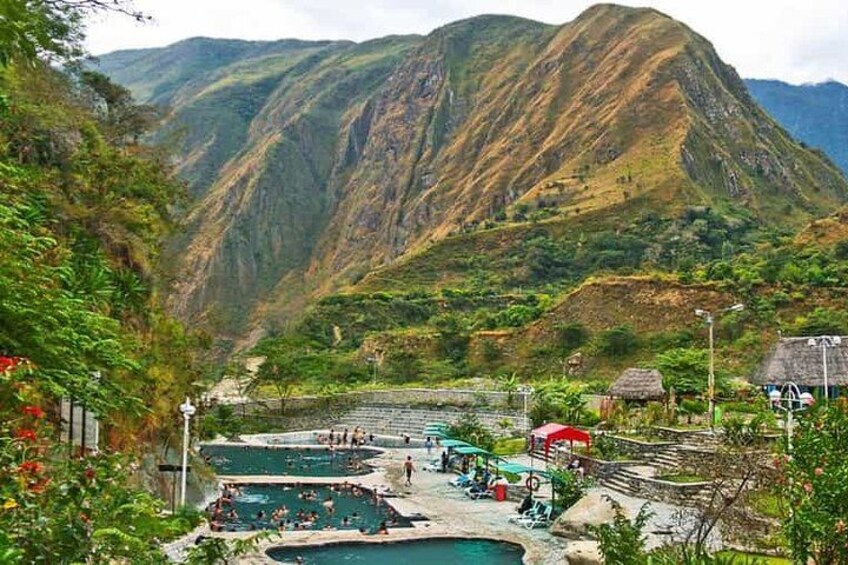 A mountainous landscape with a swimming area and thatched-roof huts. 4
