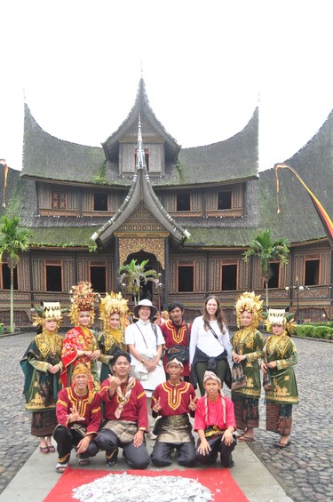 A group of people in traditional attire posing in front of a historic building with a steeply pitched roof and ornate decorations. 4