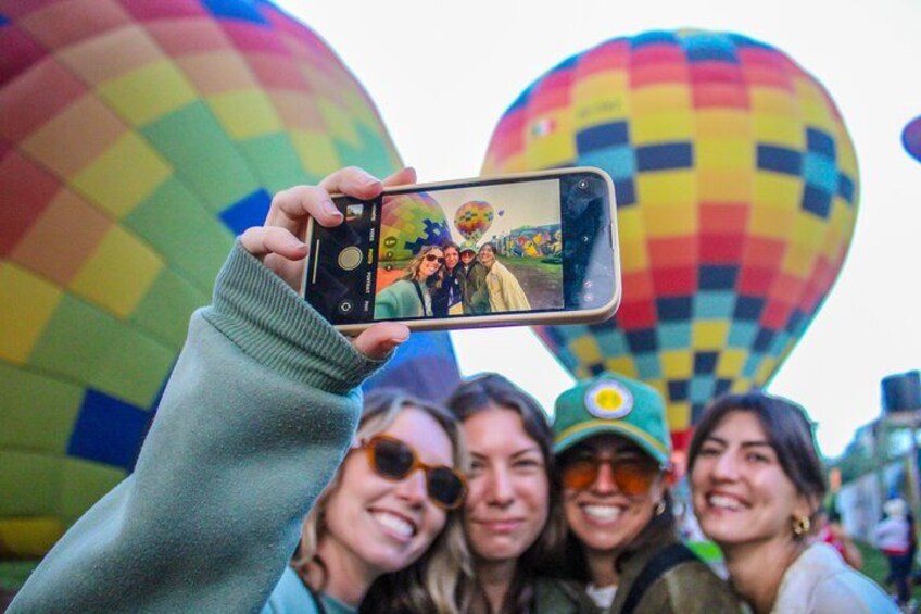 A person holding a smartphone with a photo of a group of people in front of colorful hot air balloons. 4