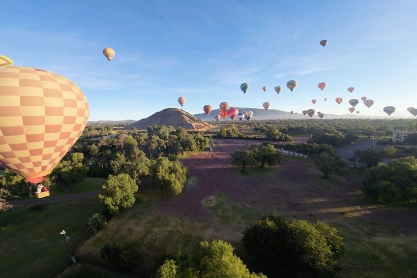 A hot air balloon festival with multiple balloons in the sky over a landscape with trees and hills. 3
