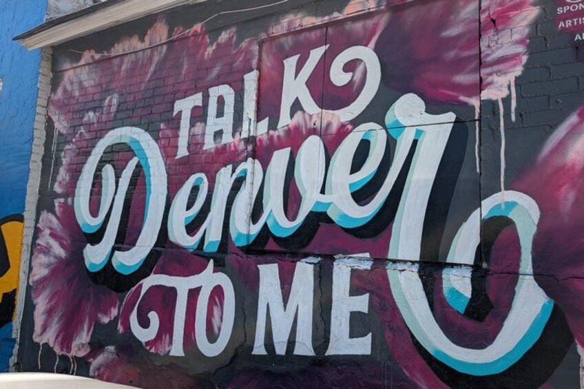 A mural with the text 'Talk to Denver to Me' on a brick wall. 1