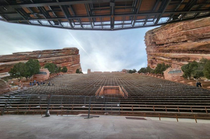 An outdoor amphitheater with tiered seating, a stage, and a natural rock formation backdrop. 4