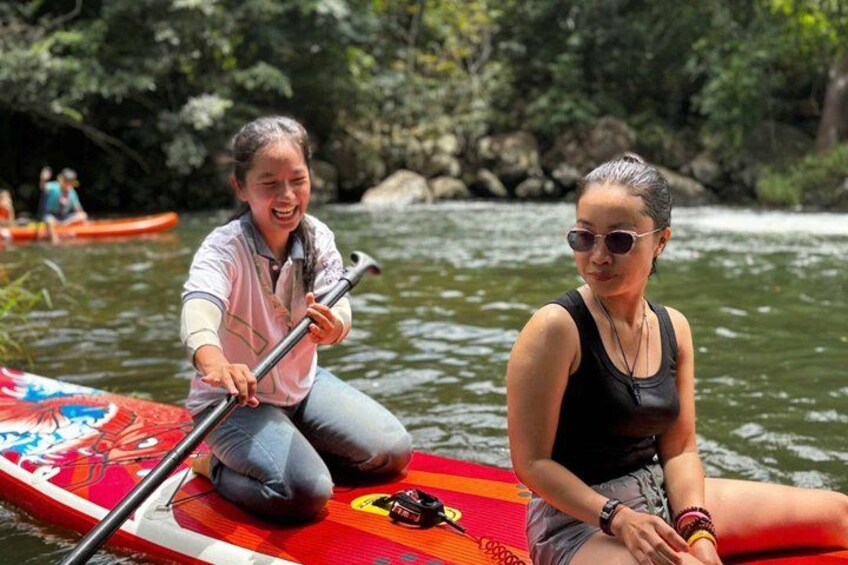 Two people on a paddleboard in a river surrounded by greenery. 5