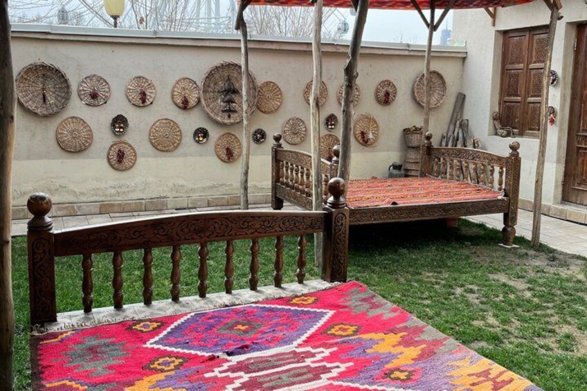 A traditional wooden bed with a colorful rug, a wall decorated with circular plates, and a wooden door in the background. 2