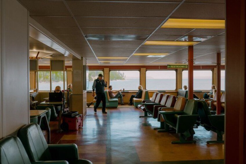 A ferry interior with rows of seats, a restrooms sign, and a person walking. 2