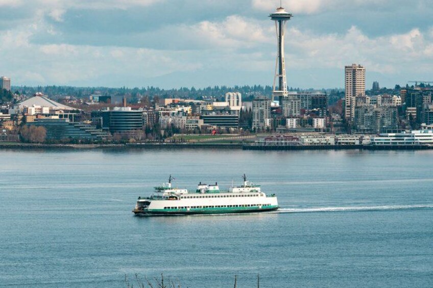 A ferry on a river with a city skyline in the background, including a prominent tower. 3