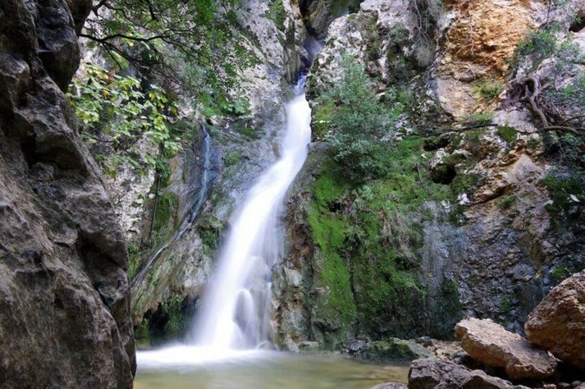 A waterfall cascading down a rocky cliff surrounded by greenery. 1