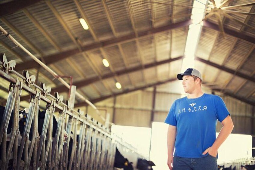 A person in a blue shirt and cap standing in a barn with metal racks and hay bales. 2