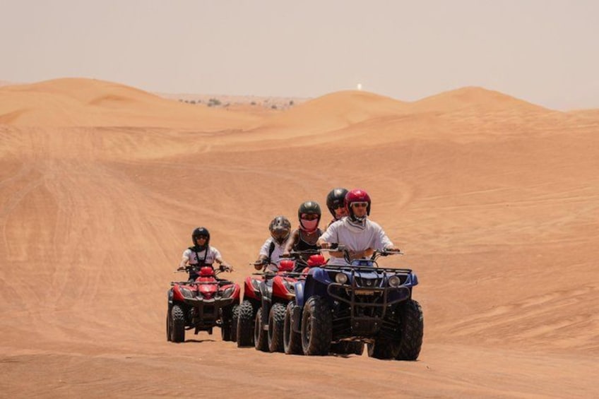 Four people on quad bikes in a desert with sand dunes. 1