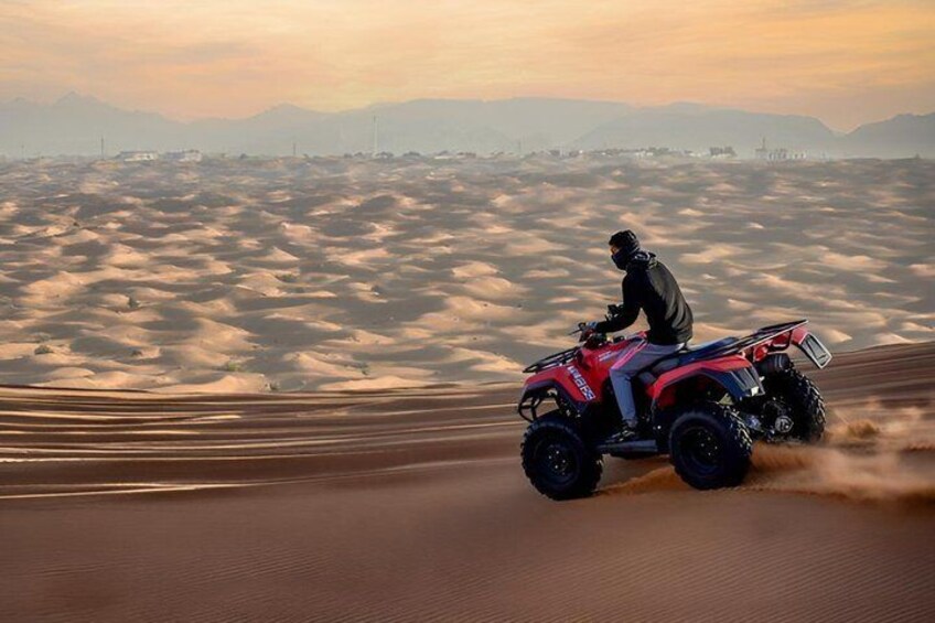 A person riding a red ATV on a sandy terrain with a mountainous backdrop. 4