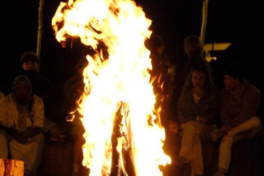 A group of people sitting around a large fire at night. 5