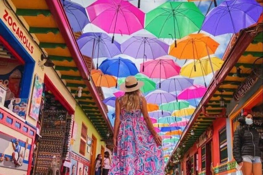 A street with colorful umbrellas and a woman in a patterned dress walking. 1