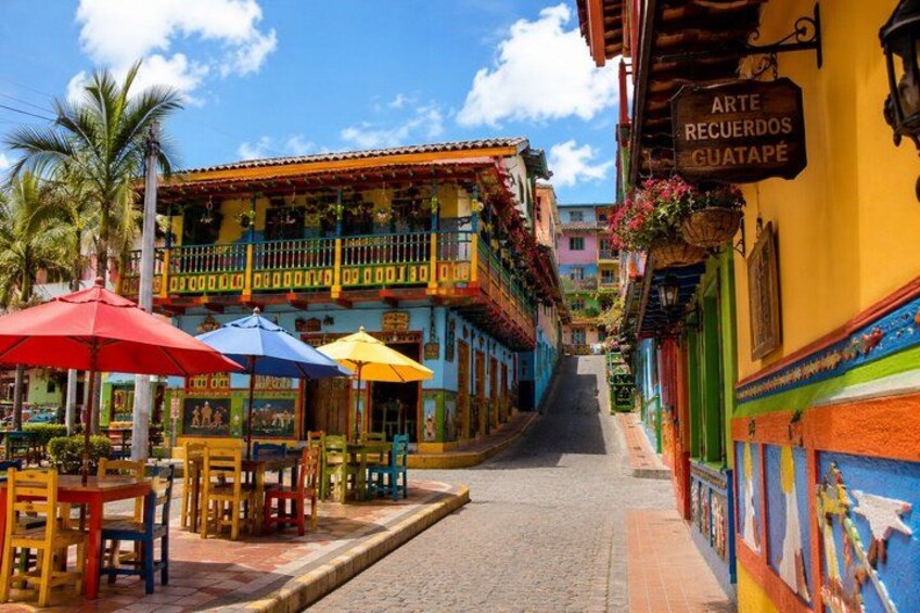 A colorful street with buildings, outdoor seating, and a sign that reads 'ARTE RECUEOS GUATAPÉ'. 3