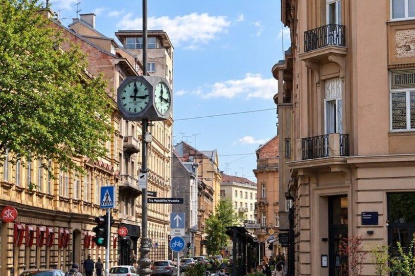 A street with buildings, a clock, traffic lights, and a pedestrian crossing. 5