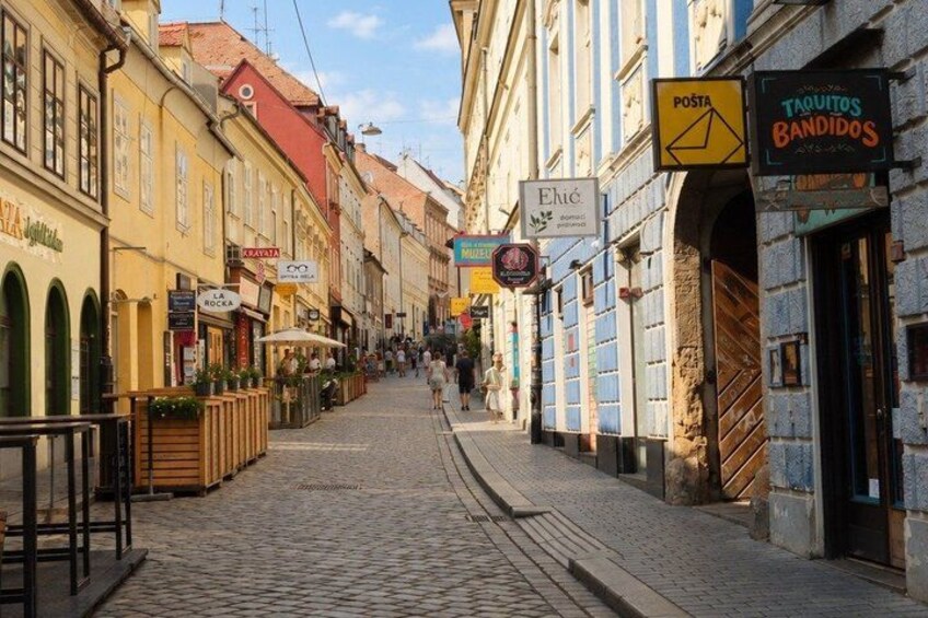 A cobblestone street lined with buildings, signs for shops, and a clear sky. 3