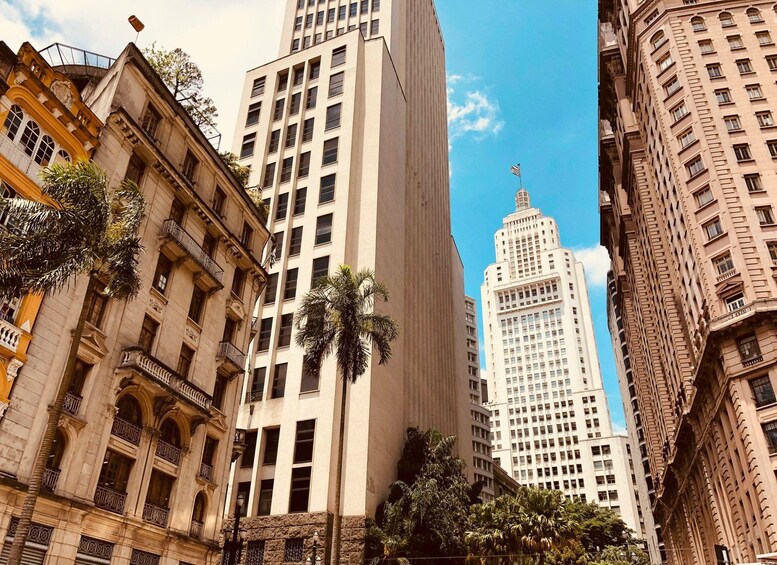 A cityscape with tall buildings, including a prominent white skyscraper with a spire, and palm trees in the foreground. 2
