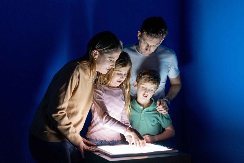 En familie på tre interagerer med en tablet i et svagt oplyst rum. 4