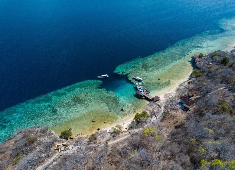 Vista aérea de una zona costera con aguas azul turquesa, una playa de arena y un pequeño muelle con barcos. 5