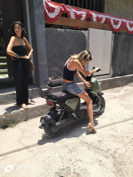 A woman sitting on a scooter, another woman standing nearby, and a building with a red and white banner. 5