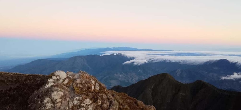 A mountain landscape with rocky outcrops and a view of distant mountains under a pinkish sky. 5